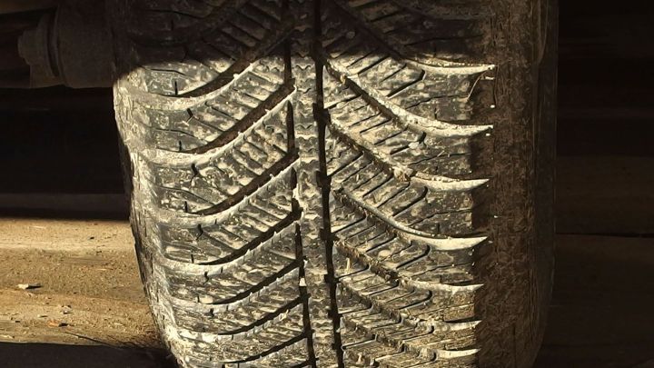 Abgenutzter Reifen zeigt tiefes Profil und Rillendetails, die die Fahrtrichtung in einer st&auml;dtischen Umgebung andeuten.