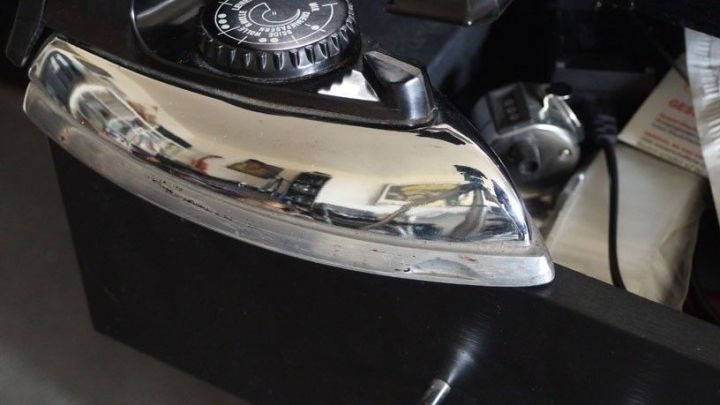 Ein gl&auml;nzender Kantenumleimer wird mit einem B&uuml;geleisen bearbeitet, w&auml;hrend er auf einer dunklen Oberfl&auml;che liegt.