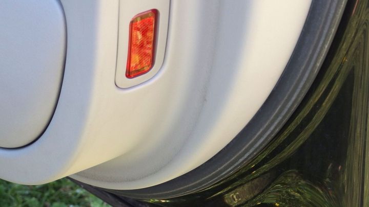 Ein Auto mit einer wei&szlig;en T&uuml;r wird mit Weichsp&uuml;ler behandelt, w&auml;hrend Gras im Hintergrund sichtbar ist.