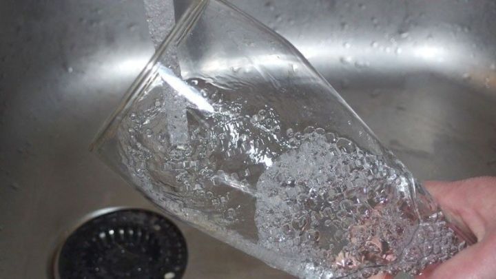 Ein Glas wird unter flie&szlig;endem Wasser gereinigt, um Schaum f&uuml;r das Bier zu entfernen, w&auml;hrend es in einem Sp&uuml;lbecken steht.