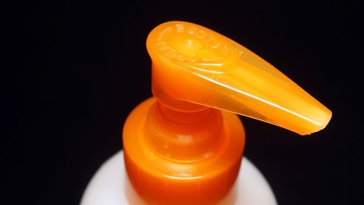 Ein Shampoo-Spender mit orangefarbenem Pumpkopf steht auf einem schwarzen Hintergrund und wartet auf die Nutzung.