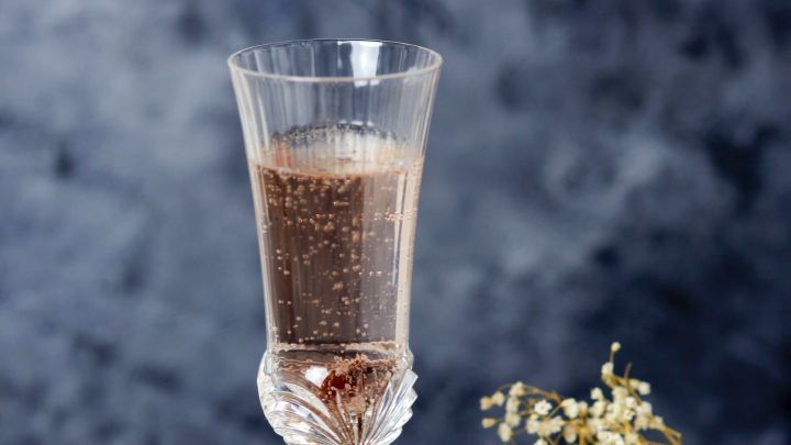 Ein stilvolles Glas Schaumwein sprudelt und steht auf einem Holzbrett, umgeben von dekorativen Bl&uuml;ten und Rosinen.