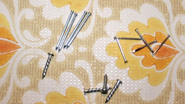 Auf einem bunten Tapetenmuster liegen mehrere N&auml;gel, die darauf warten, in die Wand geschlagen zu werden.