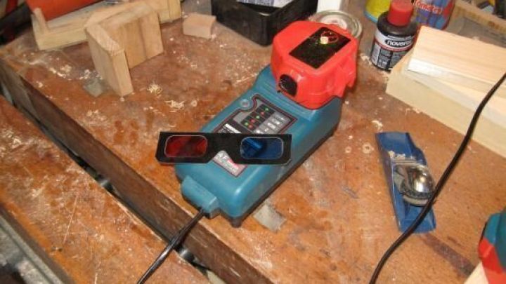 Ein blauer Werkzeuggenerator mit rotem Ladekontrolllicht steht auf einem Holzarbeitsplatz umgeben von Werkzeugen und Holzsp&auml;nen.