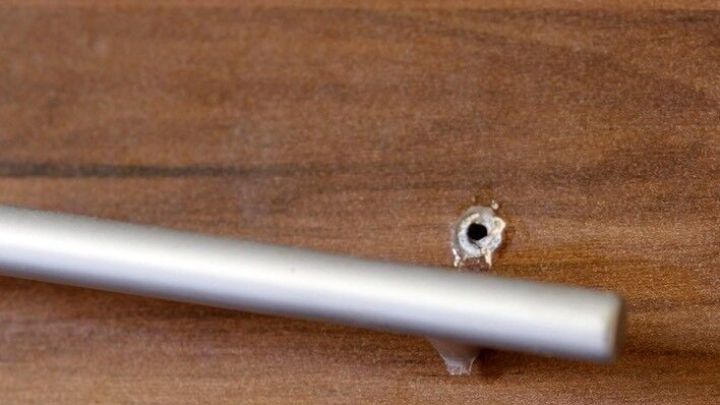 Ein beeindruckender Kunststoffm&ouml;belgriff h&auml;ngt schlaff an einer Holzplatte, w&auml;hrend er zur Reparatur positioniert ist.