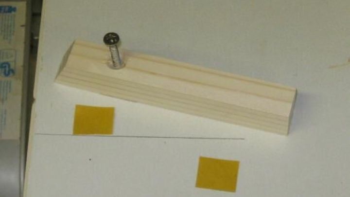 Ein Doppelklebeband auf einem Tisch h&auml;lt eine Holzleiste und einen Nagel, ideal f&uuml;r pr&auml;zises Arbeiten in der Werkstatt.
