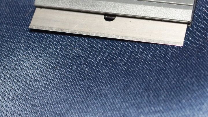 Eine Rasierklinge liegt auf einem blauen Stoff, bereit zur Reinigung, w&auml;hrend sie das Material ber&uuml;hrt.