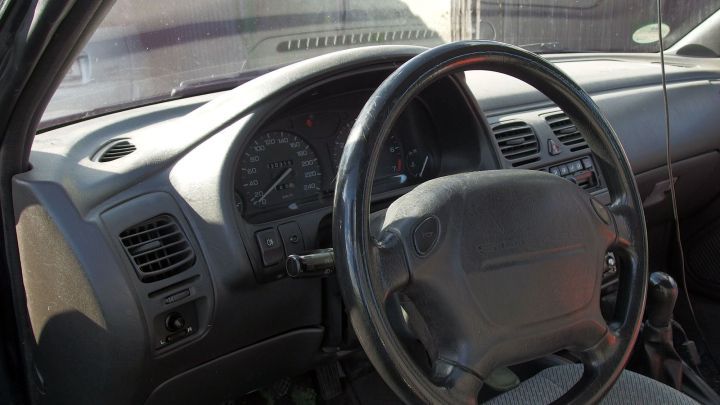 Ein Lenkrad und Armaturenbrett eines Gebrauchtwagens sind sichtbar, die Umgebung wirkt ungepflegt und abgenutzt.