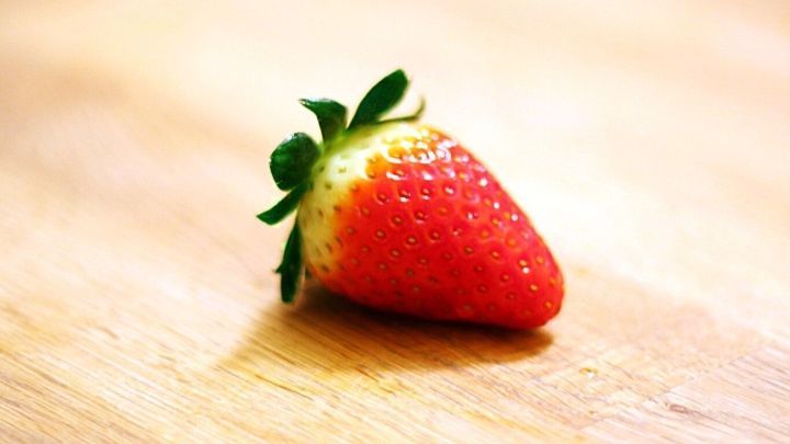 Eine saftige Erdbeere liegt auf einem hellen Holzuntergrund, ideal f&uuml;r weiche Haut und gesunde Ern&auml;hrung.