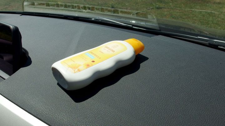 Ein Sonnencreme-Flasche liegt auf einem schwarzen Armaturenbrett. Sonnenstrahlen reflektieren die Szene im Innenraum eines Fahrzeugs.