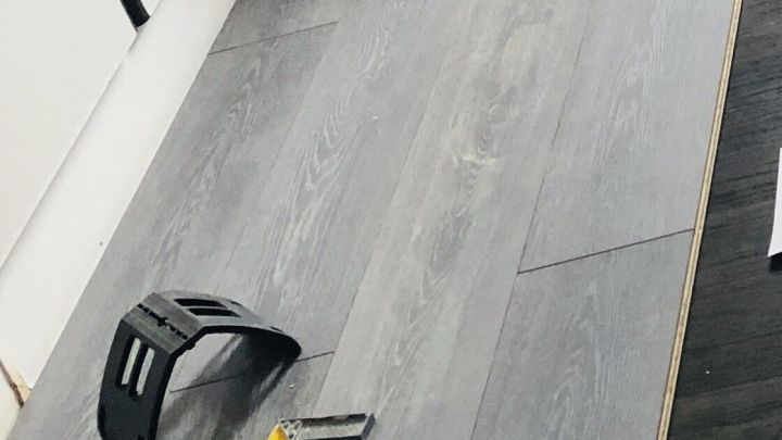 Laminatplanken liegen auf dem Boden, w&auml;hrend Werkzeug zur Verlegung in einer hellen Raumumgebung bereitliegt.