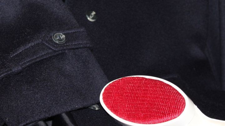 Eine Fusselb&uuml;rste mit roter Borstenseite reinigt effektiv die Kleidung neben einem schwarzen Hemd mit Kn&ouml;pfen.