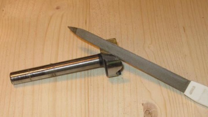 Ein Forstnerbohrer liegt auf einer Holzoberfl&auml;che, w&auml;hrend eine Nagelfeile daneben zum Sch&auml;rfen verwendet wird.