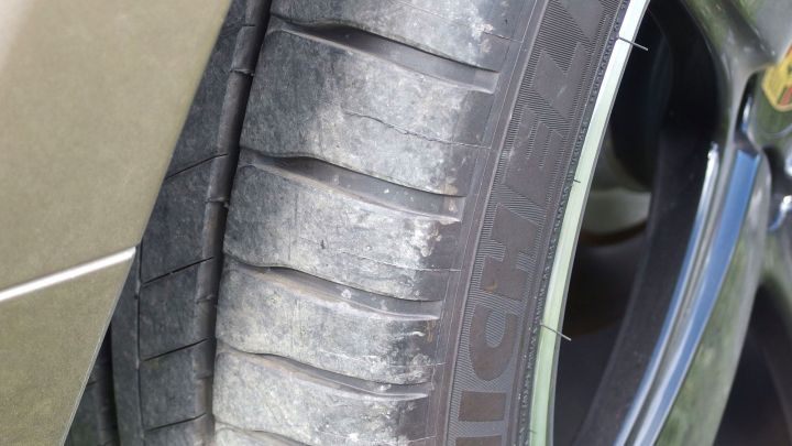 Abgenutzter Autoreifen zeigt verschlissene Profilrillen und ist Teil eines gepflegten Fahrzeugs in einer st&auml;dtischen Umgebung.