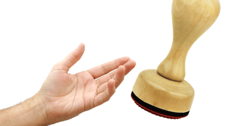 Ein Holzstempel schwebt &uuml;ber einer Hand, die bereit ist, ihn zu greifen, um den Stempel auf der Haut zu verwenden.
