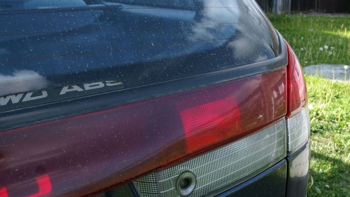 Ein gebrauchtes Auto mit sichtbarem R&uuml;cklicht steht auf einer Wiese, bereit f&uuml;r den Austausch von Autoersatzteilen.