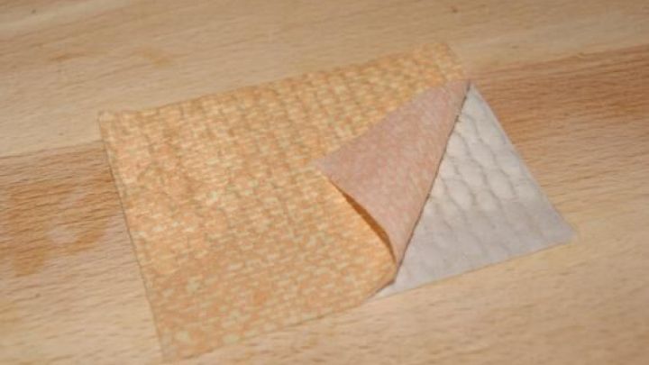 Ein St&uuml;ck orange Tapete wird auf einer Holzoberfl&auml;che leicht angehoben, um den wei&szlig; gemusterten R&uuml;ckseitenbereich zu zeigen.