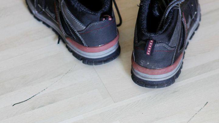 Schwarze Schuhe hinterlassen Spuren auf hellem Holzboden.