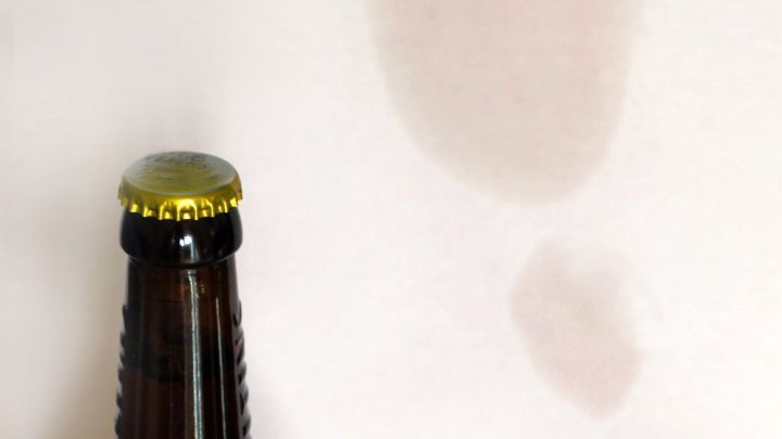 Eine Bierflasche steht neben einem hellen Hintergrund, auf dem ein kleiner Bierfleck zu sehen ist.