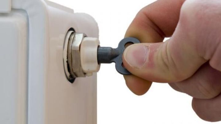 Ein Handwerker entl&uuml;ftet eine Heizung, indem er einen Entl&uuml;ftungsschl&uuml;ssel in das Ventil an der Heizk&ouml;rperseite einf&uuml;hrt.