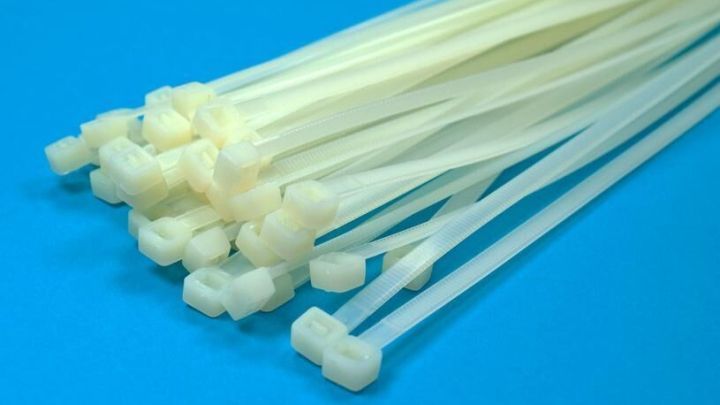 Ein B&uuml;ndel wei&szlig;er Kabelbinder liegt auf einer blauen Oberfl&auml;che, alle in gleicher Richtung ausgerichtet.