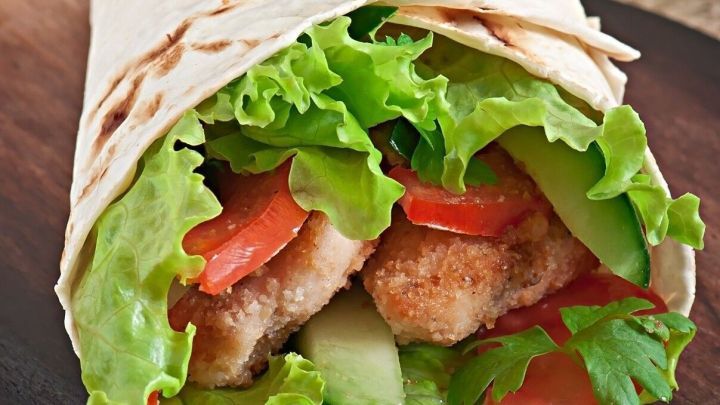 Frischer Wrap mit knackigem Salat, Tomaten und Gurken auf einem Holzbrett in einer nat&uuml;rlichen Umgebung.