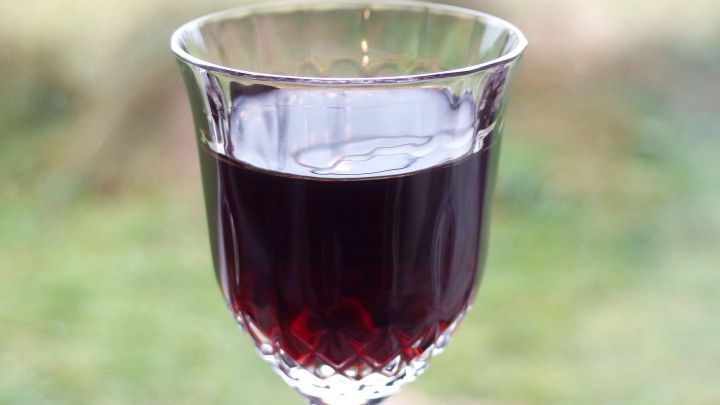 Ein Glas Kirschlik&ouml;r steht auf einem Tisch, gef&uuml;llt mit dunklem Lik&ouml;r, vor unscharfem, gr&uuml;nem Hintergrund.