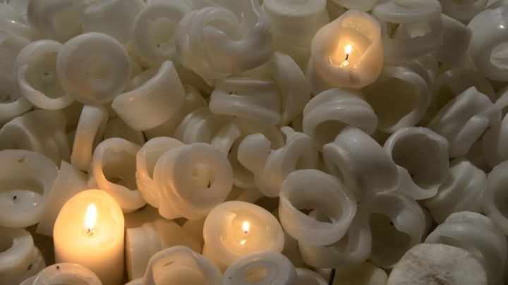 Kerzenreste leuchten in dunkler Umgebung, umgeben von weiteren wei&szlig;en Wachsresten. Drei Flammen brennen sanft.