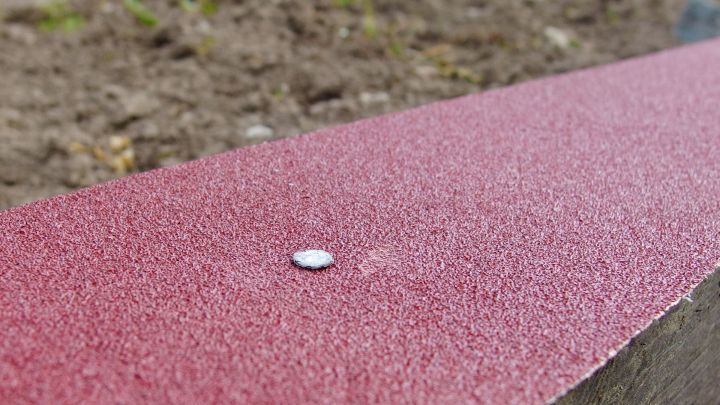 Auf einer rauen Sandpapierfl&auml;che liegt eine kleine M&uuml;nze, umgeben von Erde und Pflanzenresten im Au&szlig;enbereich.