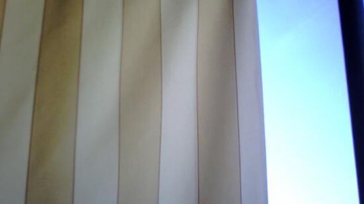 Ein beiger Sichtschutz h&auml;ngt vertikal auf einem Balkon, eingefasst von Metallstreben, mit blauem Himmel im Hintergrund.