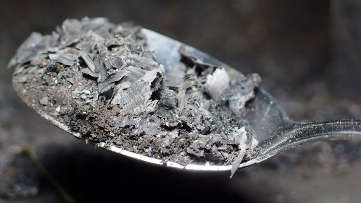 Eine Metalll&ouml;ffel mit Ru&szlig; liegt voller dunkler, feiner Partikel, bereit zur Anwendung im Pflanzenwachstum.