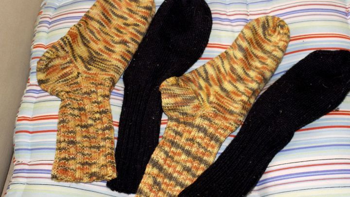 Bunte Stricksocken liegen ordentlich auf einem gestreiften Untergrund, ideal f&uuml;r warme F&uuml;&szlig;e an kalten, glatten Wintertagen.