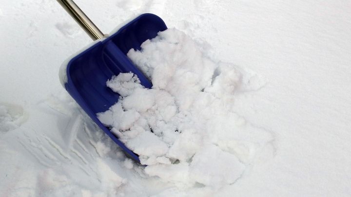 Eine Schneeschaufel liegt auf dem Boden und hebt frischen, lockeren Schnee an, um eine Fl&auml;che zu r&auml;umen.