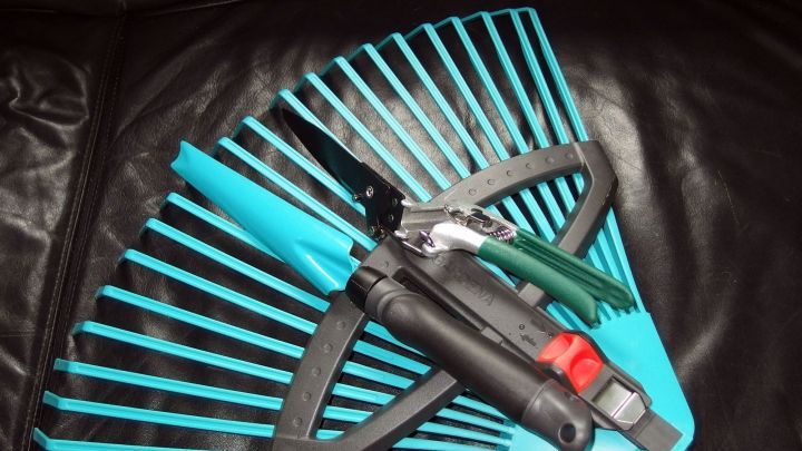 Eine gr&uuml;ne Harke und andere Gartenger&auml;te liegen auf einem schwarzen Sofa, bereit f&uuml;r dieWintervorbereitung.