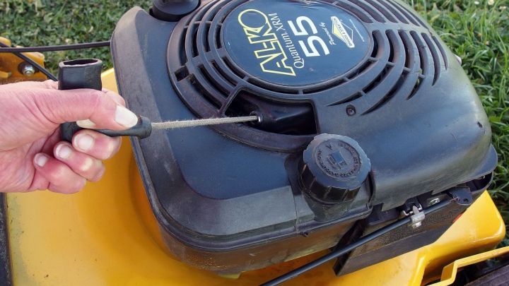 Ein Rasenm&auml;her wird mit einem Schraubendreher &uuml;berpr&uuml;ft, w&auml;hrend er auf gr&uuml;nem Gras steht, um Startprobleme zu beheben.