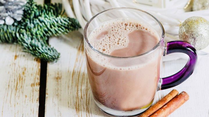 Eine Tasse hei&szlig;e Schokolade steht auf einem holzfarbenen Tisch, umgeben von festlicher Dekoration und einer Laterne.