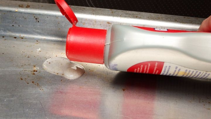 Eine Flasche mit Reinigungsmittel wird &uuml;ber ein Backblech gekippt, um festgebranntes Fett zu entfernen.