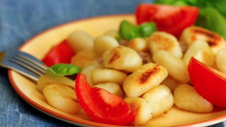 Gnocchi liegen auf einem Teller, umgeben von frischen Tomaten und Basilikum, bereit zum Servieren.