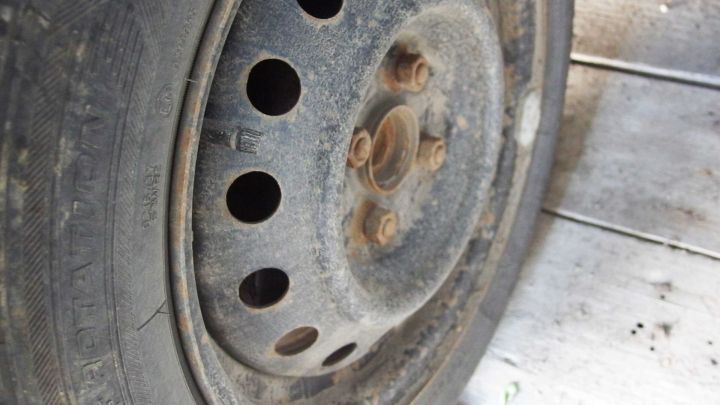 Ein schmutziger Reifen mit einem alten, rostigen Rad und mehreren Bohrungen ist auf einem staubigen Untergrund abgebildet.
