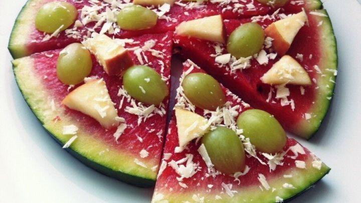 Melonen-Pizza: Wassermelonenscheiben belegt mit Weintrauben und Apfelst&uuml;cken auf einem Teller, wie eine s&uuml;&szlig;e Pizza angerichtet.