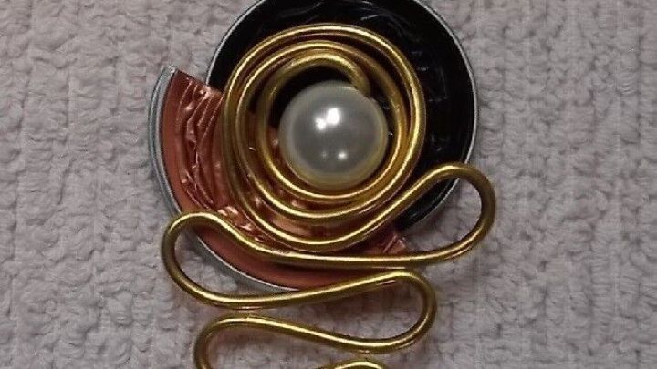 Ein Kettenanh&auml;nger aus Nespresso-Kapseln schm&uuml;ckt eine goldene Kette, mit einer Perle im Zentrum und geschwungenem Drahtdesign.