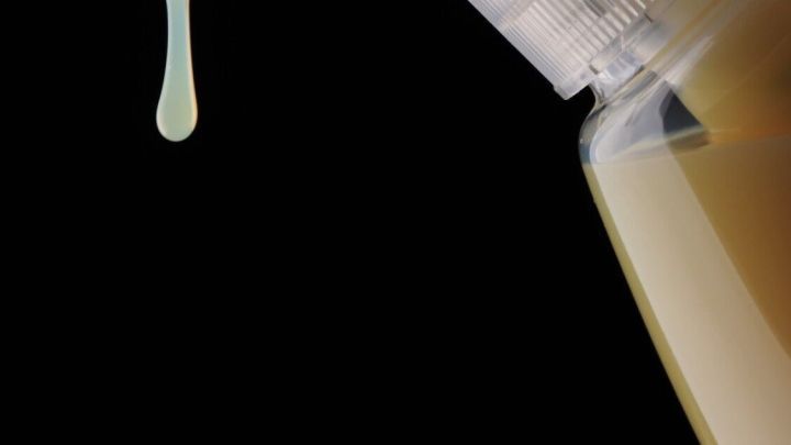 Eine Hand dr&uuml;ckt einen Seifenspender, aus dem eine Tropfen Handseife herauskommt, vor schwarzem Hintergrund.