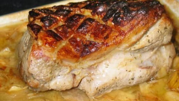 Ein Schweinebraten liegt in einer Auflaufform. Die Kruste ist braun und knusprig gebacken. Darunter kochen Zwiebeln und Gem&uuml;se.