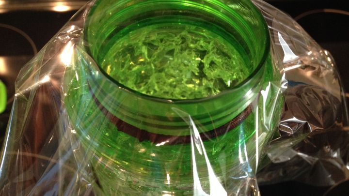 Ein gr&uuml;ner Beh&auml;lter wird mit Frischhaltefolie abgedeckt, um auslaufsicher transportiert zu werden.