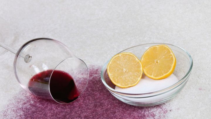 Ein umgekipptes Glas mit Rotwein versch&uuml;ttet Fl&uuml;ssigkeit auf einem Untergrund, w&auml;hrend zwei Zitronenscheiben und Salz daneben liegen.