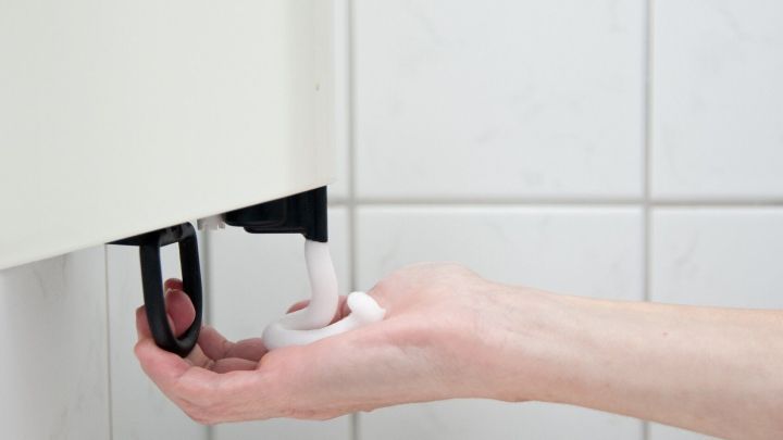 Eine Hand dr&uuml;ckt einen Deodorant-Spender in einem Badezimmer, w&auml;hrend in der Umgebung wei&szlig;e Fliesen sichtbar sind.