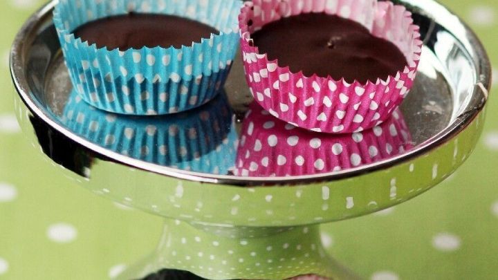 Auf einem silbernen Kuchenteller stehen zwei Erdnussbutter Cupcakes, einer in blauer, einer in rosa Papierform.