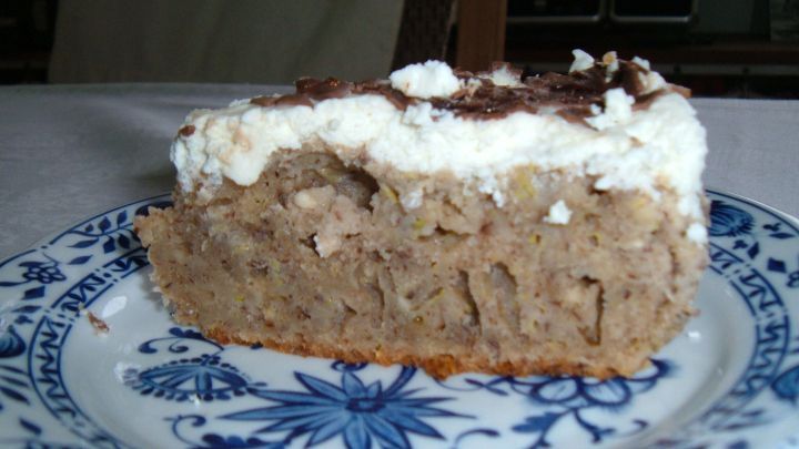 Ein St&uuml;ck Zucchini-Kuchen liegt dekorativ auf einem blau-wei&szlig;en Teller, bedeckt mit einer cremigen Schicht, im Esszimmer.