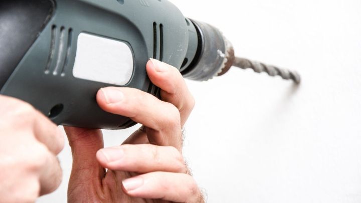 Eine Hand h&auml;lt einen Bohrer, der ein Loch in eine Wand bohrt, um eine Befestigung oder Montage vorzunehmen.