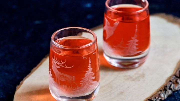 Zwei kleine Gl&auml;ser mit rotem Getr&auml;nk stehen auf einem Holzbrett, umgeben von einer dunklen, ruhigen Umgebung.